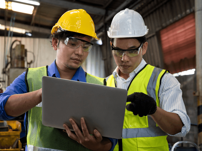 Two workers discussing something over a laptop in a factory space.